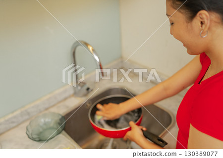 A woman is diligently cleaning her cookware in the kitchen sink using soap and water 130389077