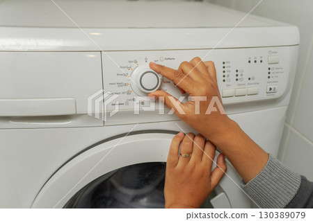 User is setting the washing machine dial to achieve the optimal laundry cycle User is setting the washing machine dial to achieve the optimal laundry cycle 130389079