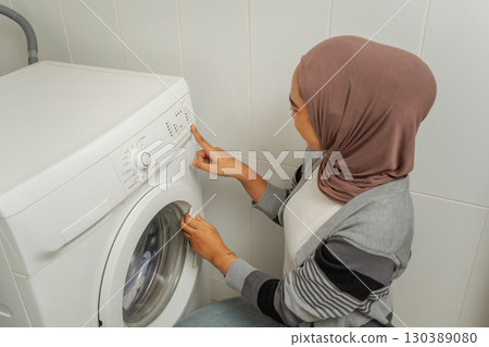 A woman is diligently using a modern washing machine in her bright laundry room 130389080