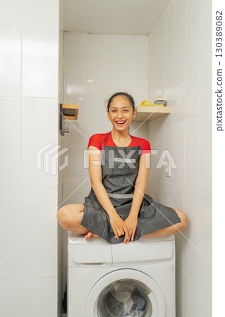 A Playful Woman Posing Cheerfully on a Washing Machine in a Stylish Kitchen 130389082