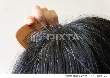 Close-up image of gray hair and flyaway hairs on the top of the head of a middle-aged woman Close-up image of gray hair and flyaway hairs on the top of the head of a middle-aged woman 130389177