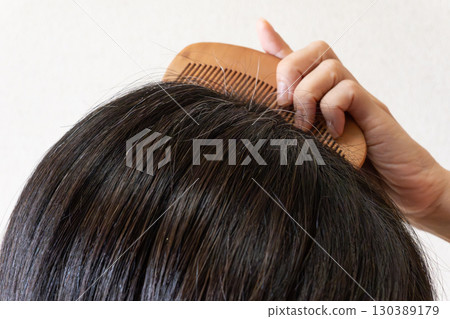 Close-up image of gray hair and flyaway hairs on the top of the head of a middle-aged woman 130389179
