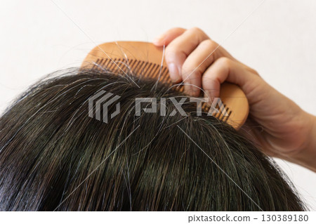Close-up image of gray hair and flyaway hairs on the top of the head of a middle-aged woman 130389180