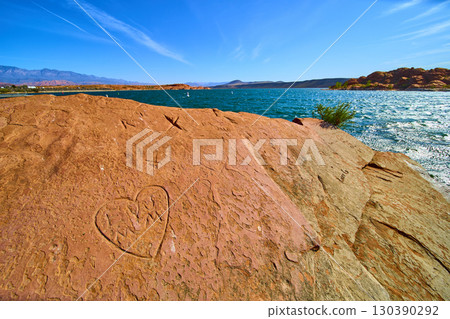 Red Rock Heart Carving by Desert Lake with Blue Water Low Eye Level Perspective 130390292