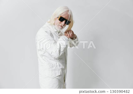 Stylish elderly man with white hair and sunglasses wearing a white outfit, confidently posing in a modern studio with a minimalistic gray background Stylish elderly man with white hair and sunglasses wearing a white outfit, confidently posing in a modern studio with a minimalistic gray background 130390482