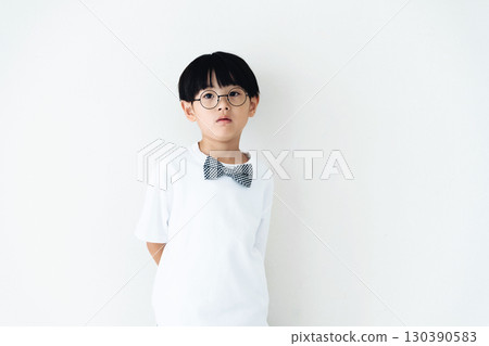 Elementary school boy standing in front of a white wall Elementary school boy standing in front of a white wall 130390583