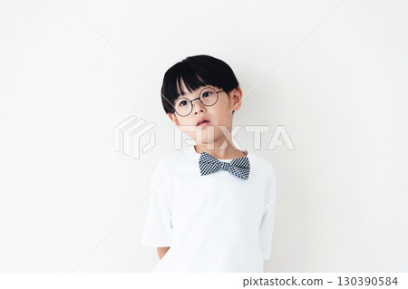 Elementary school boy standing in front of a white wall Elementary school boy standing in front of a white wall 130390584