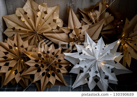 3d craft snowflakes with garland lights. Sustainableminded Christmas cozy home handmade decoration. Tutorial for making do it yourself craft paper lunch bags and hot glue. Seasonal activity for kids 130390689