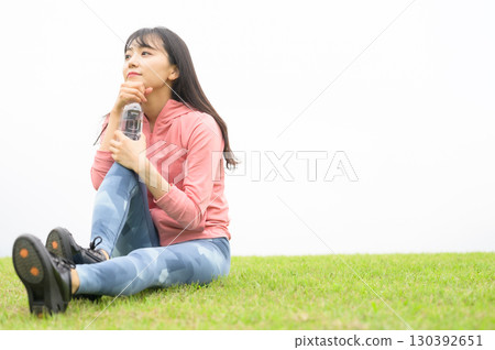 A woman hydrating after exercise on the grass 130392651