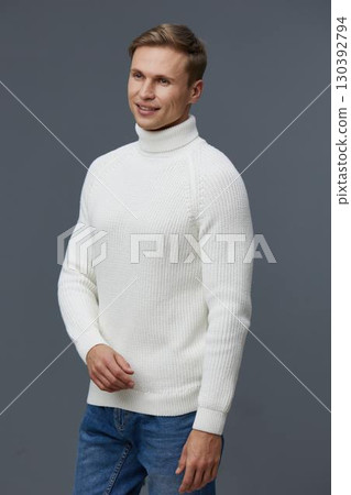 Man wearing white turtleneck sweater standing against gray background, smiling, casual clothing, autumn fashion, cozy winter outfit, relaxed pose, studio portrait. People lifestyle concept 130392794
