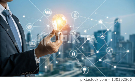 A businessman holds a glowing light bulb symbolizing innovation and new ideas, connected to a digital network representing technology and business solutions 130392806