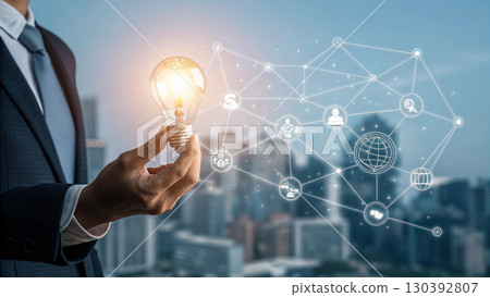 A businessman holds a glowing light bulb symbolizing innovation and new ideas, connected to a digital network representing technology and business solutions A businessman holds a glowing light bulb symbolizing innovation and new ideas, connected to a digital network representing technology and business solutions 130392807