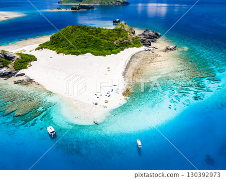 Drone shot of Kabi Island. Tourists are on the white sand beach. Parasols, boats, and sabani boats are moored. 130392973