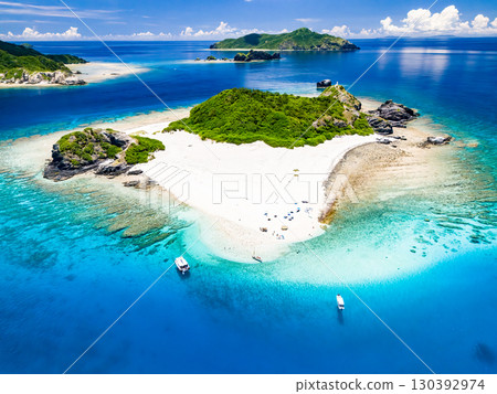 Drone shot of Kabi Island. Tourists are on the white sand beach. Parasols, boats, and sabani boats are moored. 130392974