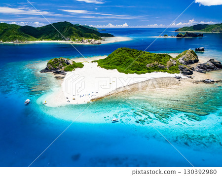 Drone shot of Kabi Island. Tourists are on the white sand beach. Parasols, boats, and sabani boats are moored. Drone shot of Kabi Island. Tourists are on the white sand beach. Parasols, boats, and sabani boats are moored. 130392980