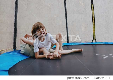 Happy boy playing joyfully on a trampoline with friends, showcasing fun and laughter in a vibrant outdoor setting, perfect for children's playtime themes. 130394007