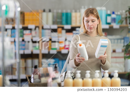 Girl in autumn clothes choosing skin cream at drugstore Girl in autumn clothes choosing skin cream at drugstore 130394203