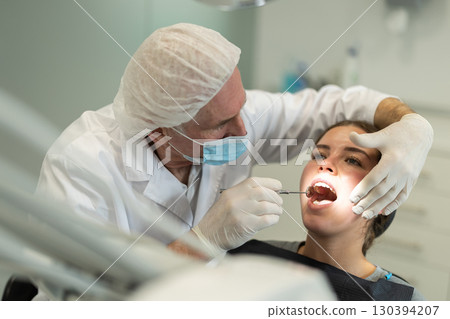 Elderly male dentist examining female patient 130394207