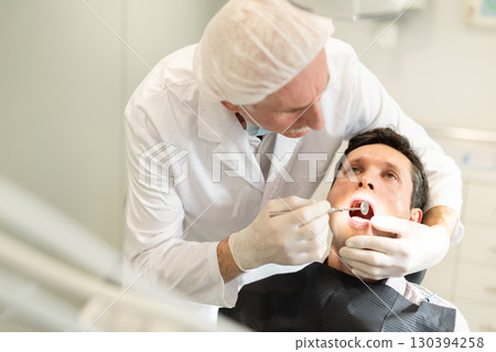 Elderly male dentist examining male patient 130394258
