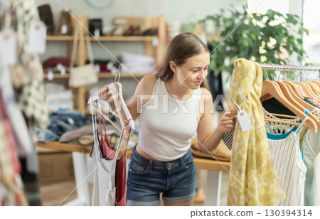 Positive teenage girl choosing something for summer in clothing store Positive teenage girl choosing something for summer in clothing store 130394314