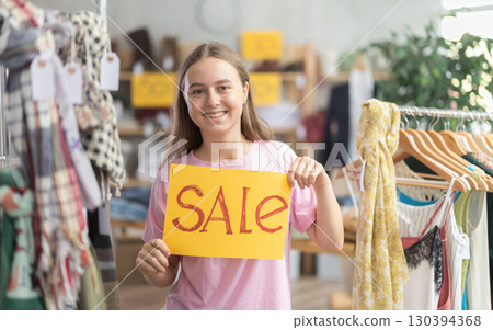 Young teenage girl holding a sign saying Sale in the interior of fashion store Young teenage girl holding a sign saying Sale in the interior of fashion store 130394368