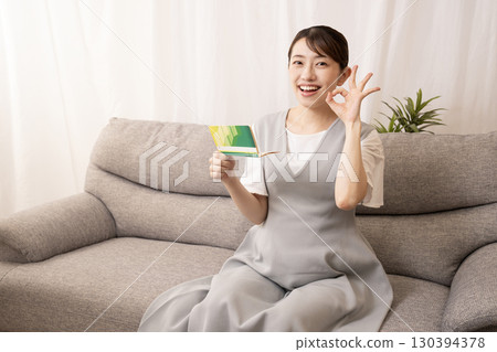 一名懷孕八個月的婦女坐在沙發上,手裡拿著一本存摺 一名懷孕八個月的婦女坐在沙發上,手裡拿著一本存摺 130394378