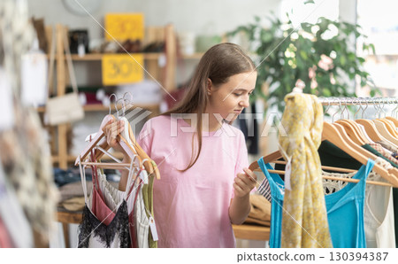Girl chooses a set of clothes for summer. Visitor to the boutique examines the new summer collection of clothes 130394387