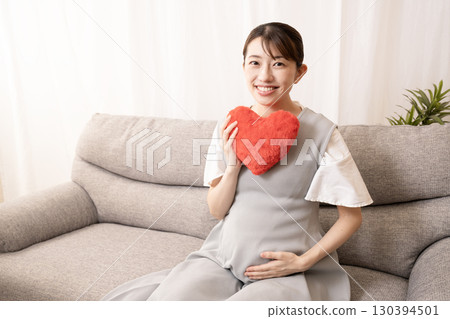 懷孕八個月的女人坐在沙發上，手裡拿著一顆紅心 130394501