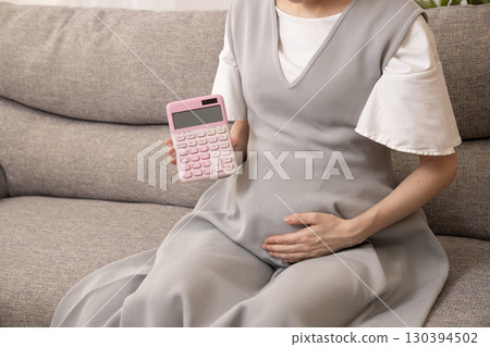懷孕八個月的女子坐在沙發上，手上拿著計算機 130394502