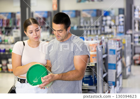 Husband buyer with paint container in hand consults with wife and examines can of enamel dye 130394623