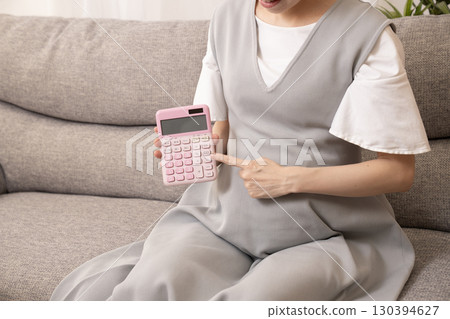 Eight-month pregnant woman sitting on a sofa and holding a calculator Eight-month pregnant woman sitting on a sofa and holding a calculator 130394627