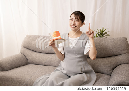 An eight-month pregnant woman sitting on a sofa and holding a bankbook An eight-month pregnant woman sitting on a sofa and holding a bankbook 130394629