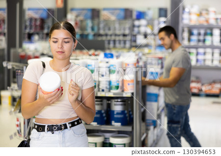 Woman buys paint tin in paintwork material store for carrying out internal finishing work on object Woman buys paint tin in paintwork material store for carrying out internal finishing work on object 130394653
