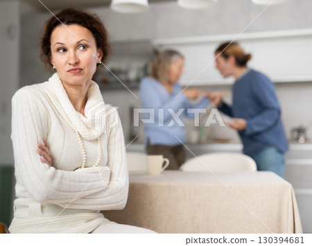 Frustrated woman sitting in kitchen during quarrel between her husband and elderly mother. 130394681