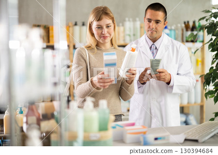 Young woman choosing cream while pharmacist offering in drugstore 130394684