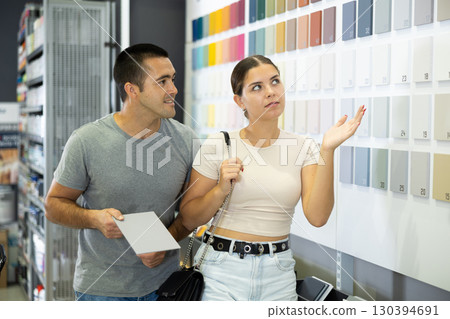 Near stand with samples paint, palette of colors of coating, couple examines showcase 130394691