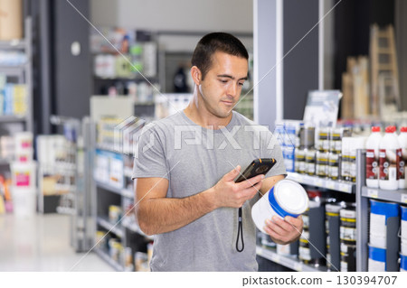 Man examines product in paint shop and scans QR code on label of enamel dye for painting walls. Man examines product in paint shop and scans QR code on label of enamel dye for painting walls. 130394707