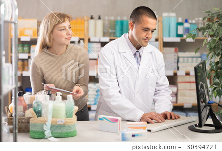 Man pharmacist is working at computer, communicate with girl customer Man pharmacist is working at computer, communicate with girl customer 130394721