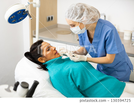 Cosmetologist giving lip injections of botulinum toxin to woman patient 130394725
