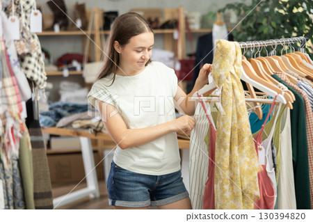 Positive teenage girl choosing something for summer in clothing store Positive teenage girl choosing something for summer in clothing store 130394820
