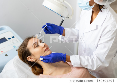 Woman cosmetician giving face injections of botulinum toxin for young woman 130394891