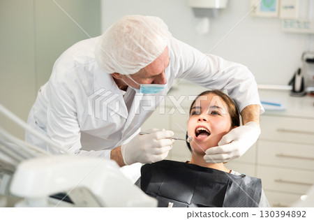 Elderly male dentist examining female patient 130394892