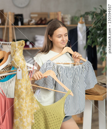 Positive teenage girl choosing something for summer in clothing store 130394987