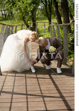 Couple adjusts shoes during wedding celebration on a wooden bridge Couple adjusts shoes during wedding celebration on a wooden bridge 130395281