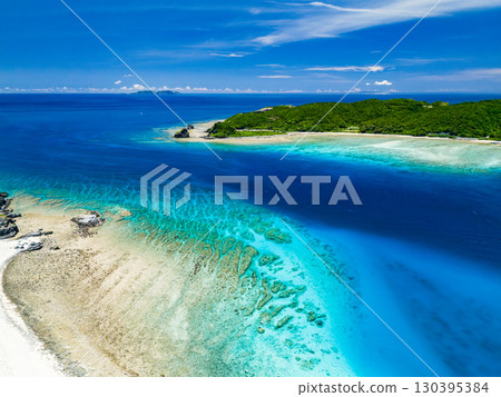 Drone shot of Kabi Island. Tourists are landing on the white sand beach. Parasols are set up, and boats and sabani boats are moored. Drone shot of Kabi Island. Tourists are landing on the white sand beach. Parasols are set up, and boats and sabani boats are moored. 130395384