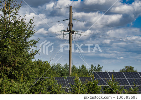Solar Panels Under Power Lines with Trees and Cloudy Sky 130395695