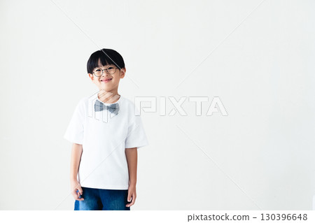Elementary school boy standing in front of a white wall Elementary school boy standing in front of a white wall 130396648