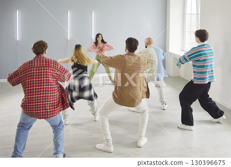 Modern indoor dance studio, diverse group of dancing young people actively following trainer woman Modern indoor dance studio, diverse group of dancing young people actively following trainer woman 130396675