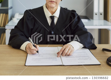 Female judge, wearing robe, writing document, handling legal process, in formal office, paperwork Female judge, wearing robe, writing document, handling legal process, in formal office, paperwork 130396682