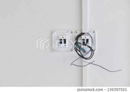 Closeup detail of an unfinished electrical switch installation during house renovation. exposed wire shows hazardous moment in construction process on white wall Closeup detail of an unfinished electrical switch installation during house renovation. exposed wire shows hazardous moment in construction process on white wall 130397501